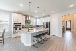 Una cocina moderna con armarios blancos, una isla grande con taburetes de bar y electrodomésticos de acero inoxidable.