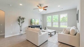 Ein geräumiges Wohnzimmer mit zwei weißen Sofas, einem Couchtisch, einem Deckenventilator und einem großen Fenster mit Jalousien.