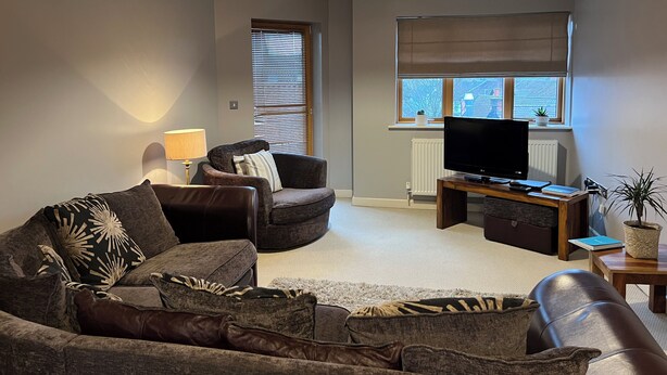 A modern living room with a sofa, armchair, and a TV on a wooden stand. - Tranquil, pet friendly apartment In Norwich city centre (Norwich)