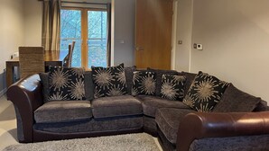 A modern living room with a sectional sofa, a dining table, and a large window with curtains. - Tranquil, pet friendly apartment In Norwich city centre (Norwich)