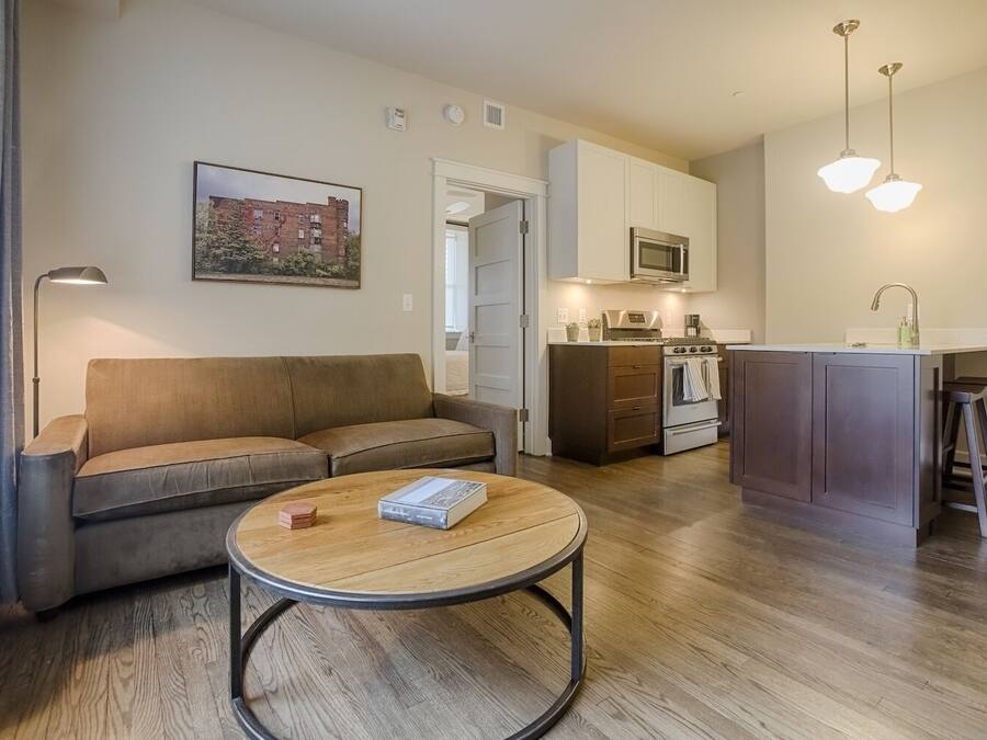 A modern living room with a sofa, coffee table, and kitchen area with a microwave and stove.