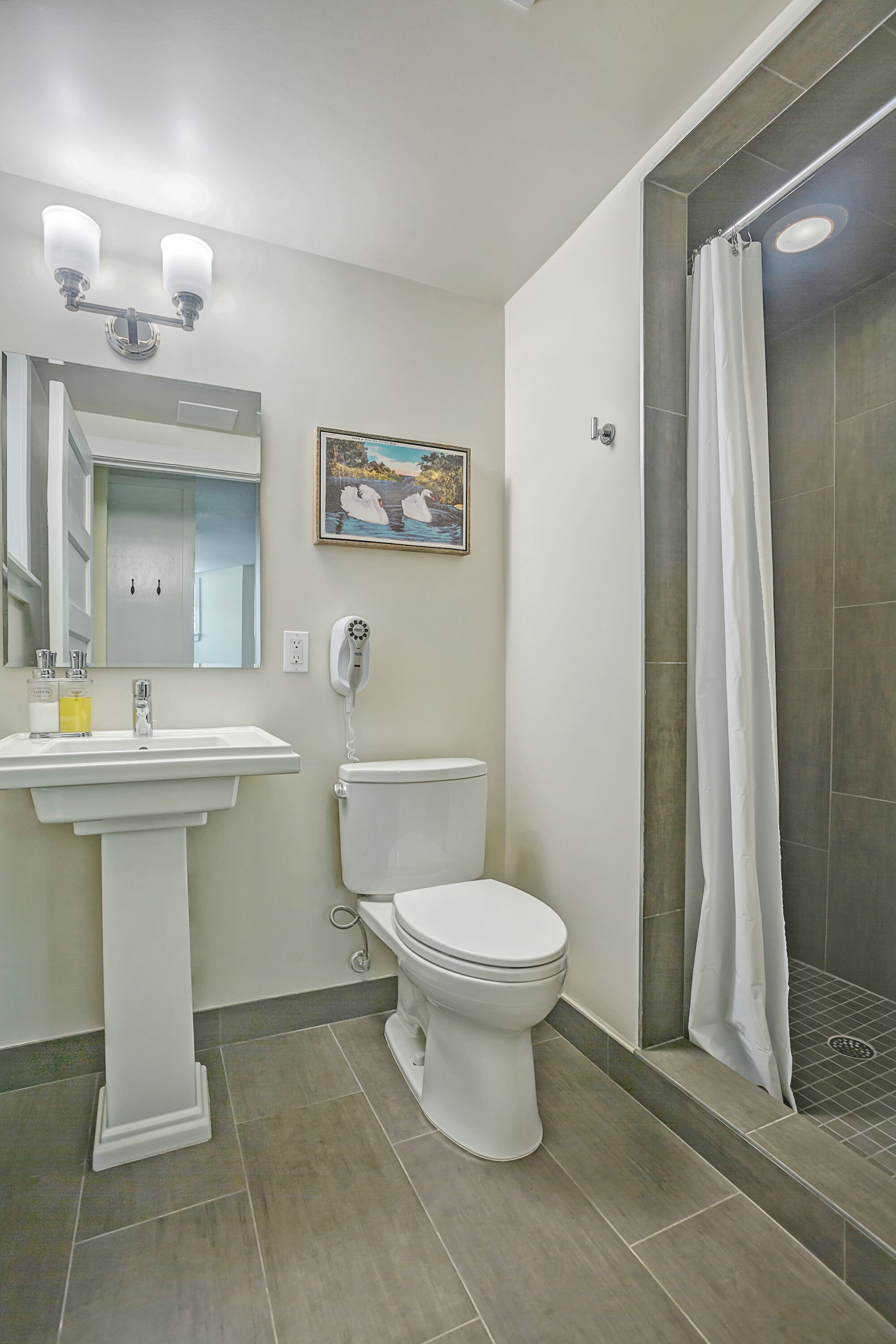 Un baño con lavamanos pedestal, inodoro, ducha con cortina y lámpara de pared.
