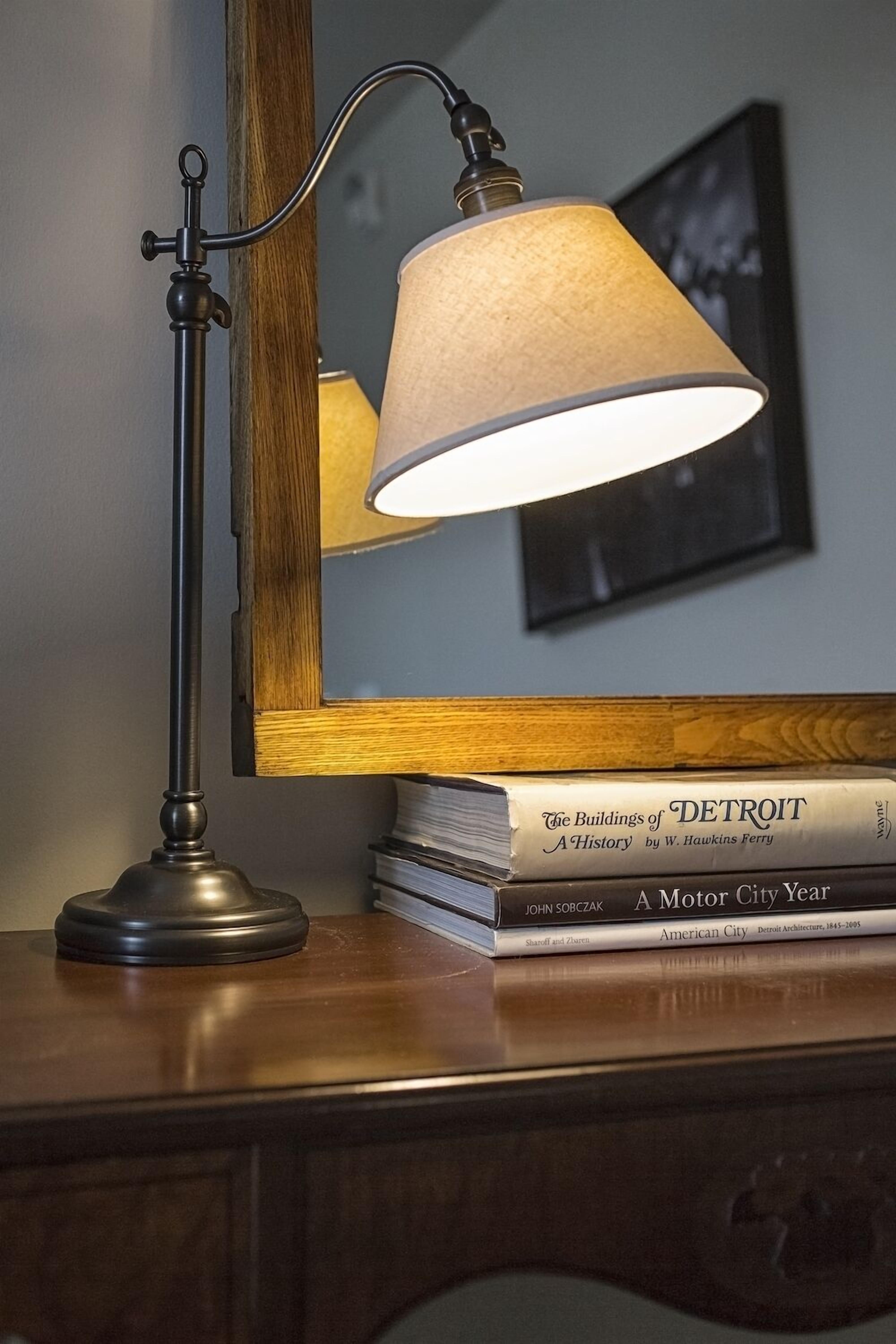 A desk lamp with a reflective surface, a stack of books, and a mirror.