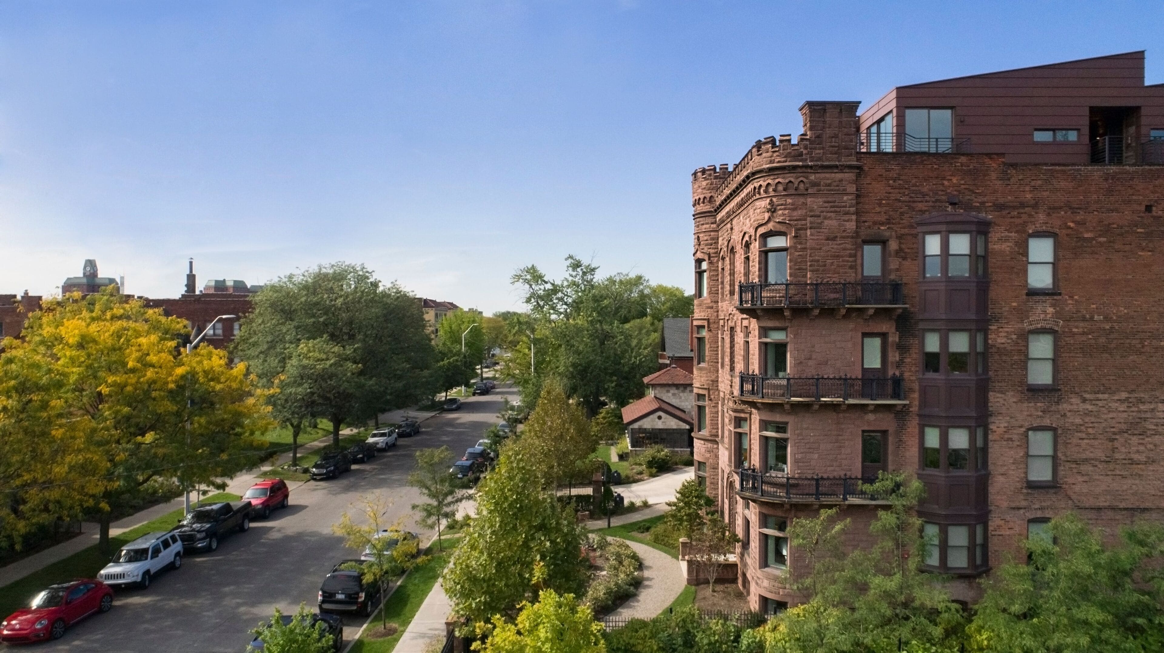 A multi-story brick building with a central courtyard, surrounded by trees and parked cars.