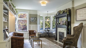 A cozy living room with a fireplace, comfortable seating, and large windows offering a view of trees.