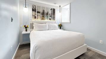 A modern bedroom with a large bed, a window with a view of a bridge, and a nightstand with a vase of flowers.