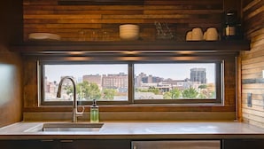 A kitchen with a large window, a stainless steel sink, and wooden paneling.