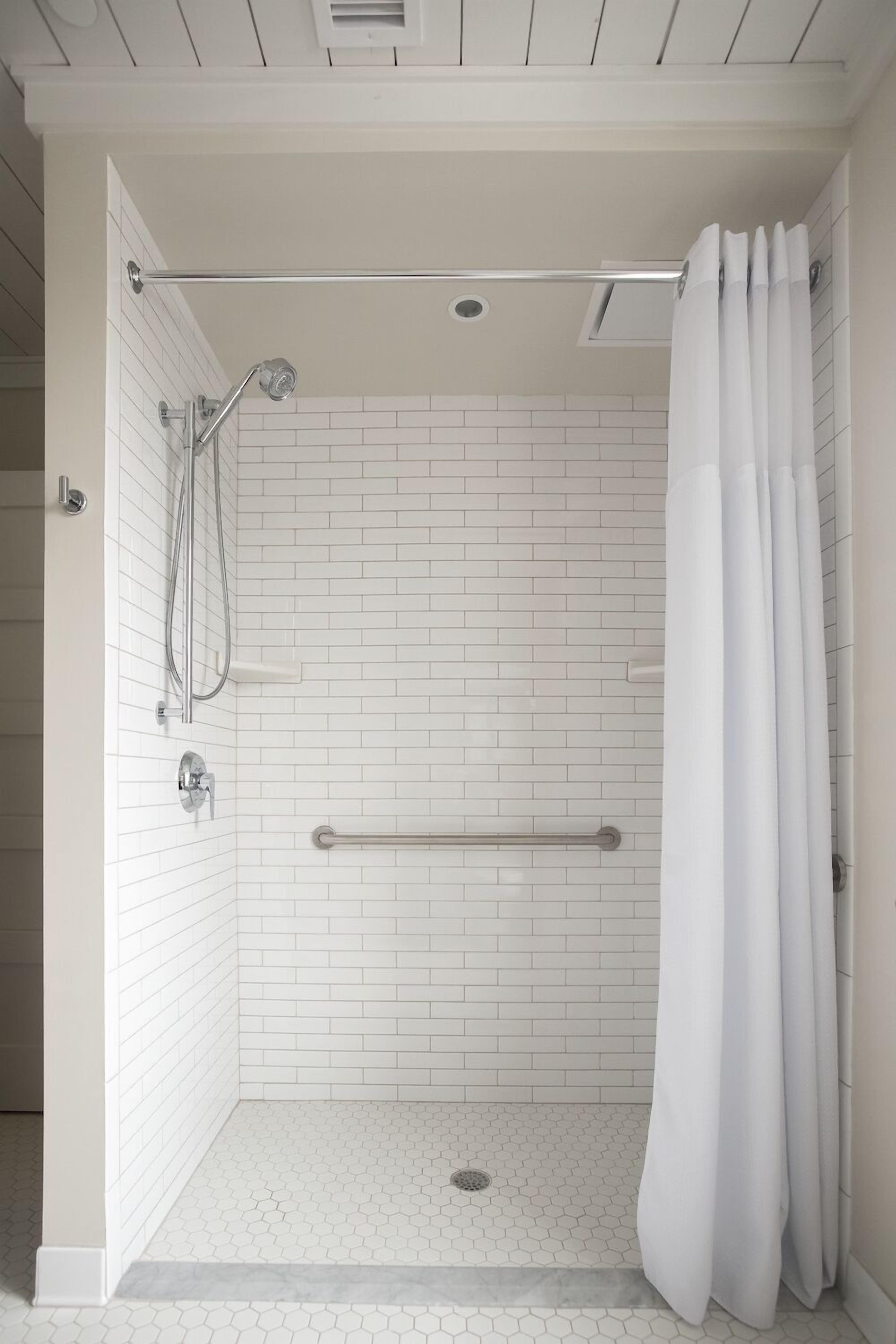 Een douche met witte tegels, een handgreep, douchekop en een gordijn.