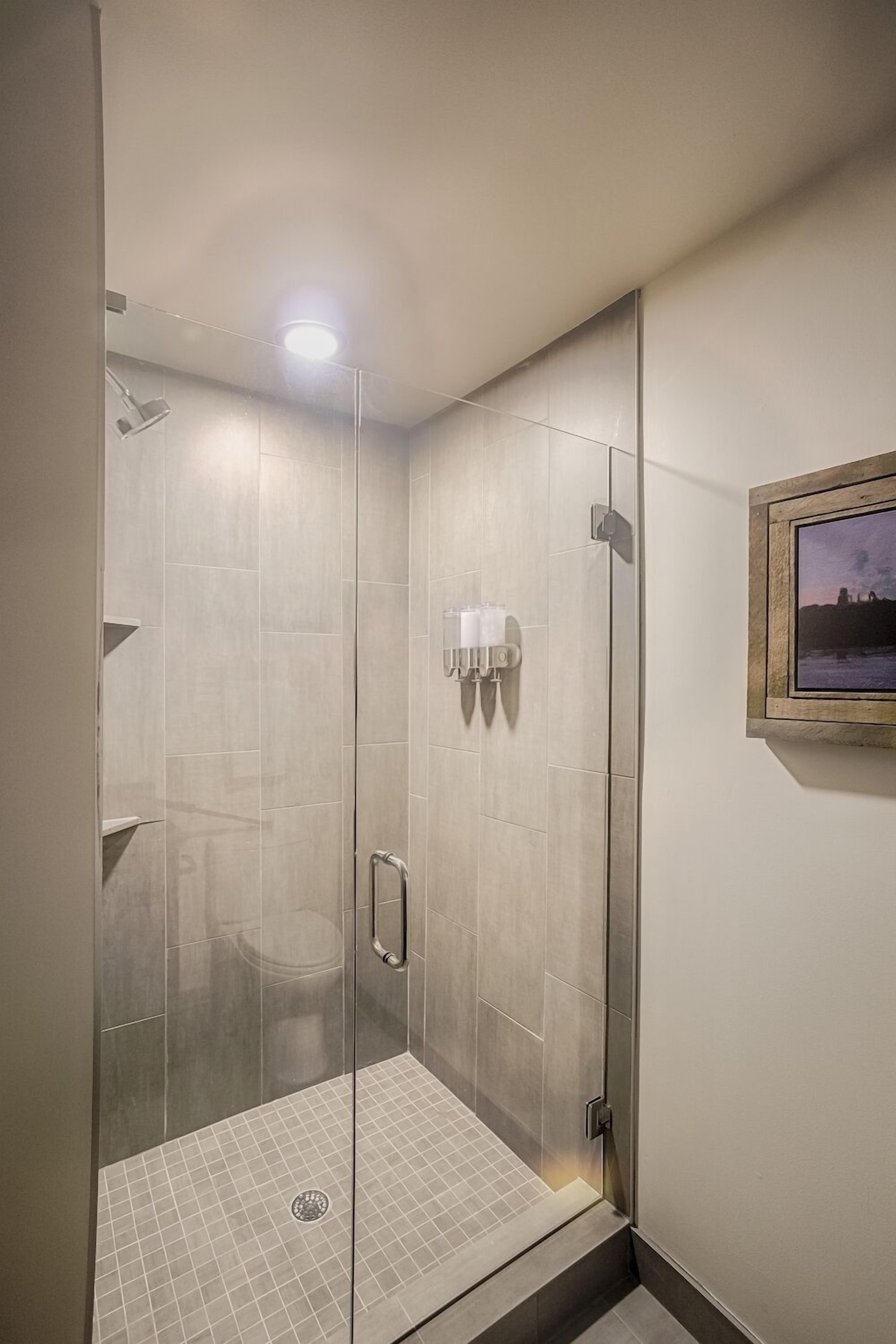 Uma área de chuveiro moderna com porta de vidro, piso ladrilhado e luminária na parede.