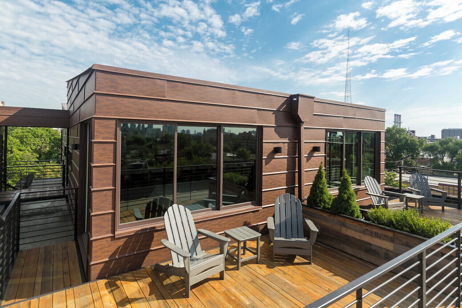 Un edificio moderno con ventanas amplias y una terraza de madera con sillas Adirondack.