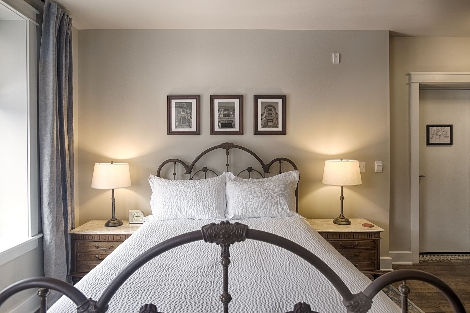 A neatly arranged bedroom with a bed, two bedside tables with lamps, and three framed pictures on the wall.