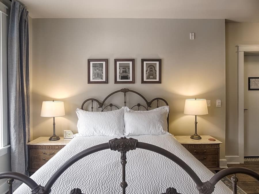 Quarto bem arrumado com uma cama, duas mesas de cabeceira com abajures e três quadros na parede.