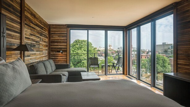 A modern bedroom with a large bed, a sofa, and a balcony with a city view.