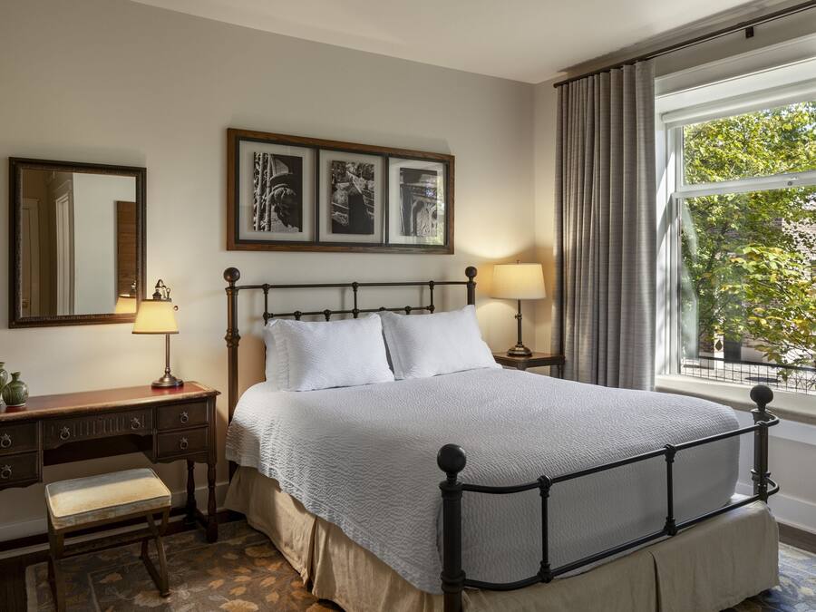 Un dormitorio ordenado con cama, mesitas de noche, cómoda y ventana con cortinas.