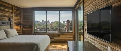 A modern bedroom with a large window, wooden paneling, a bed, and a TV.