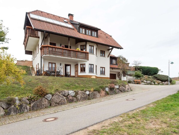 A two-story house with a balcony, a stone wall, and a paved driveway. - Apartment in Kleines Wiesental (Kleines Wiesental - Raich)