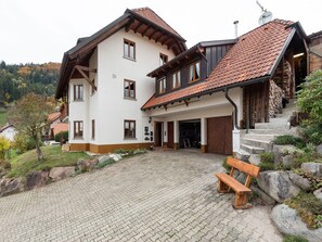 A two-story house with a tiled roof, a wooden bench, and a paved driveway. - Apartment in Kleines Wiesental (Kleines Wiesental - Raich)