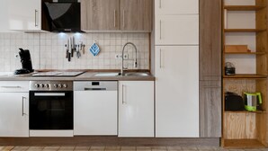 A modern kitchen with white cabinets, a built-in oven, a stove, a sink, and a black range hood. - Apartment in Kleines Wiesental (Kleines Wiesental - Raich)