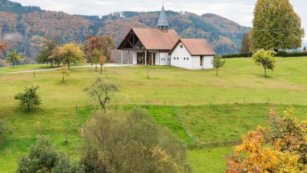 A small white church with a red roof and a bell tower, surrounded by a grassy field and trees with autumn foliage. - Apartment in Kleines Wiesental (Kleines Wiesental - Raich)