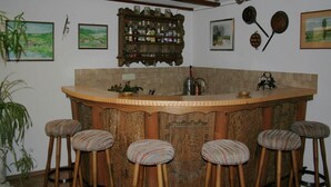 Un espace bar avec un comptoir en bois, quatre tabourets et une étagère remplie de bouteilles.