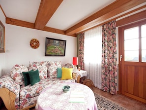 A cozy living room with a floral sofa, a small table with a bowl, a painting, and a wooden door.