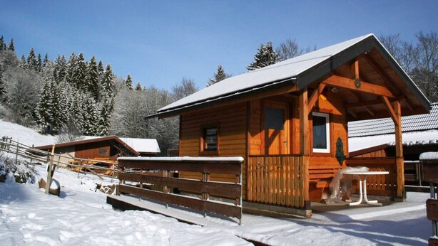 Une cabane en bois avec une véranda couverte, une petite table et un banc.