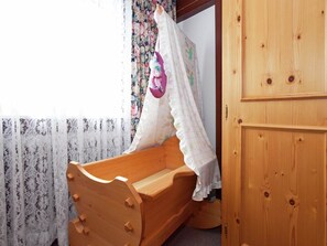 A wooden crib with a floral curtain backdrop and a wooden wardrobe. - Ferienwohnung im Schwarzwald mit Garten (Dachsberg-Urberg)