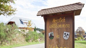 Une enseigne d’accueil en bois portant l’inscription « Herzlich willkommen in Urberg » et ornée de deux symboles représentant des blasons.