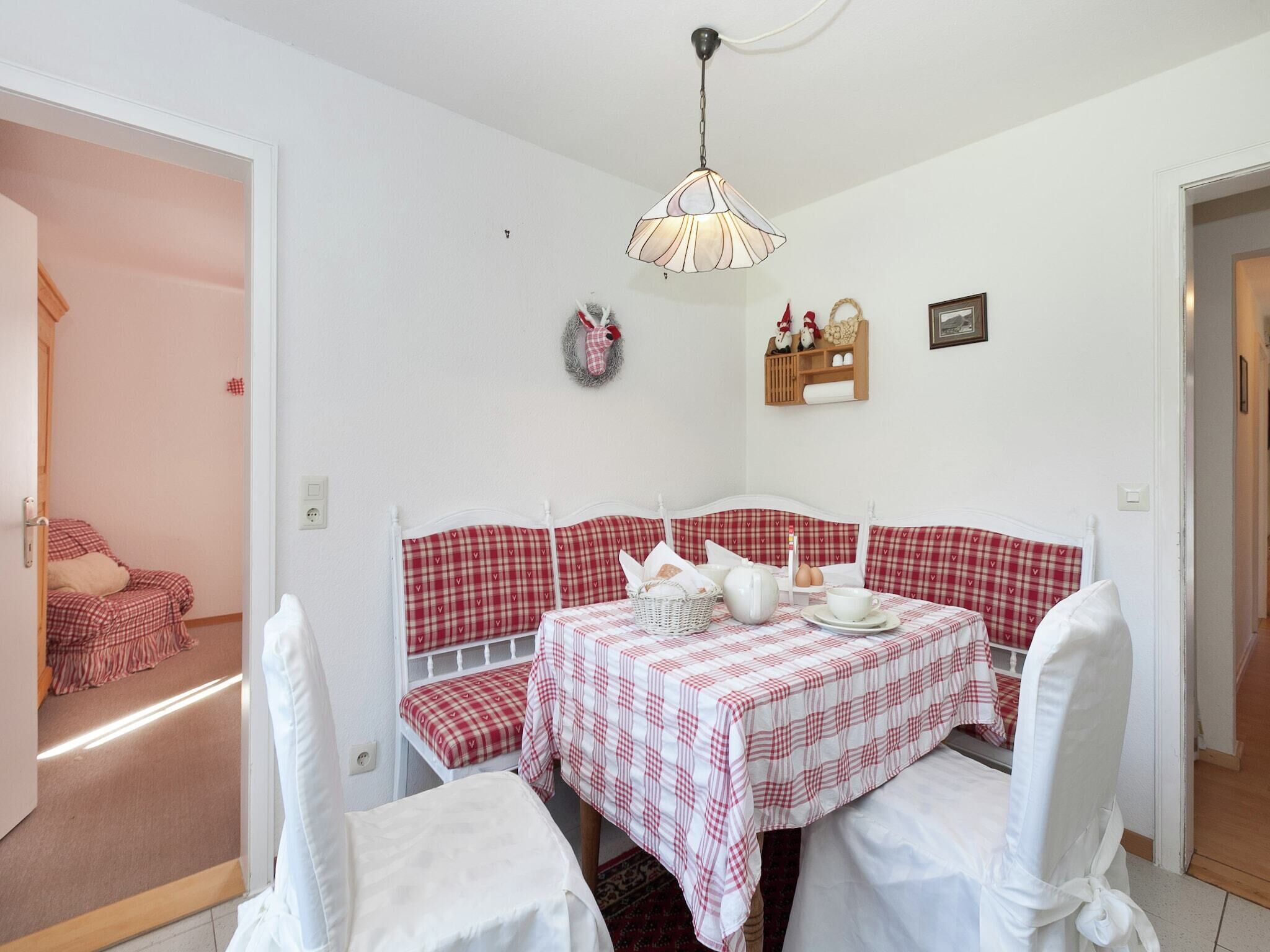 A cozy room with a checkered sofa and matching chairs, a table set with a white tablecloth, and a decorative wall shelf.