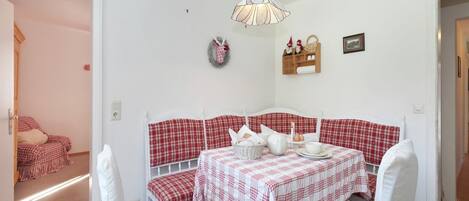 A cozy room with a checkered sofa and matching chairs, a table set with a white tablecloth, and a decorative wall shelf.