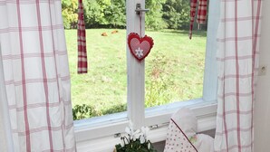 Een kamer met een raam dat uitkijkt op een tuin, gordijnen, een hartvormige decoratie en een plant.