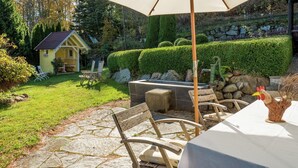 Een terras met stenen vloer, tuinmeubilair en een grote parasol.