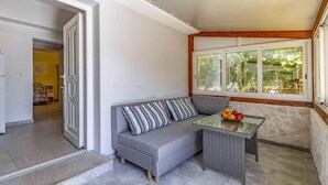 A modern living room with a grey sofa, striped cushions, a glass coffee table with fruit, and a large window with a view of greenery.
