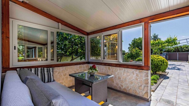 A sunroom with a stone wall, a glass table, and a sofa.