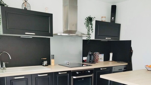 Una cocina moderna con armarios oscuros, una campana extractora de acero inoxidable, un horno integrado y una isla central con taburetes.