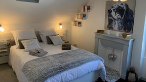 Un dormitorio con cama, mesitas de noche, chimenea, un cuadro y una lámpara en el techo.