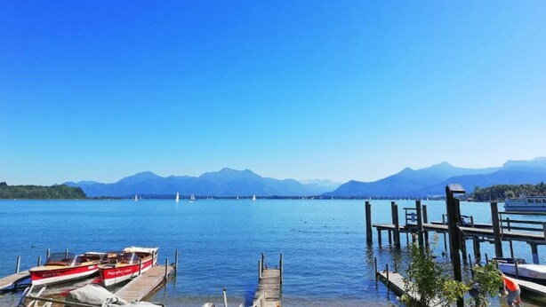 A calm lake with boats docked at a wooden pier, surrounded by mountains. - Ferienwohnung in Ruhpolding (Ruhpolding)
