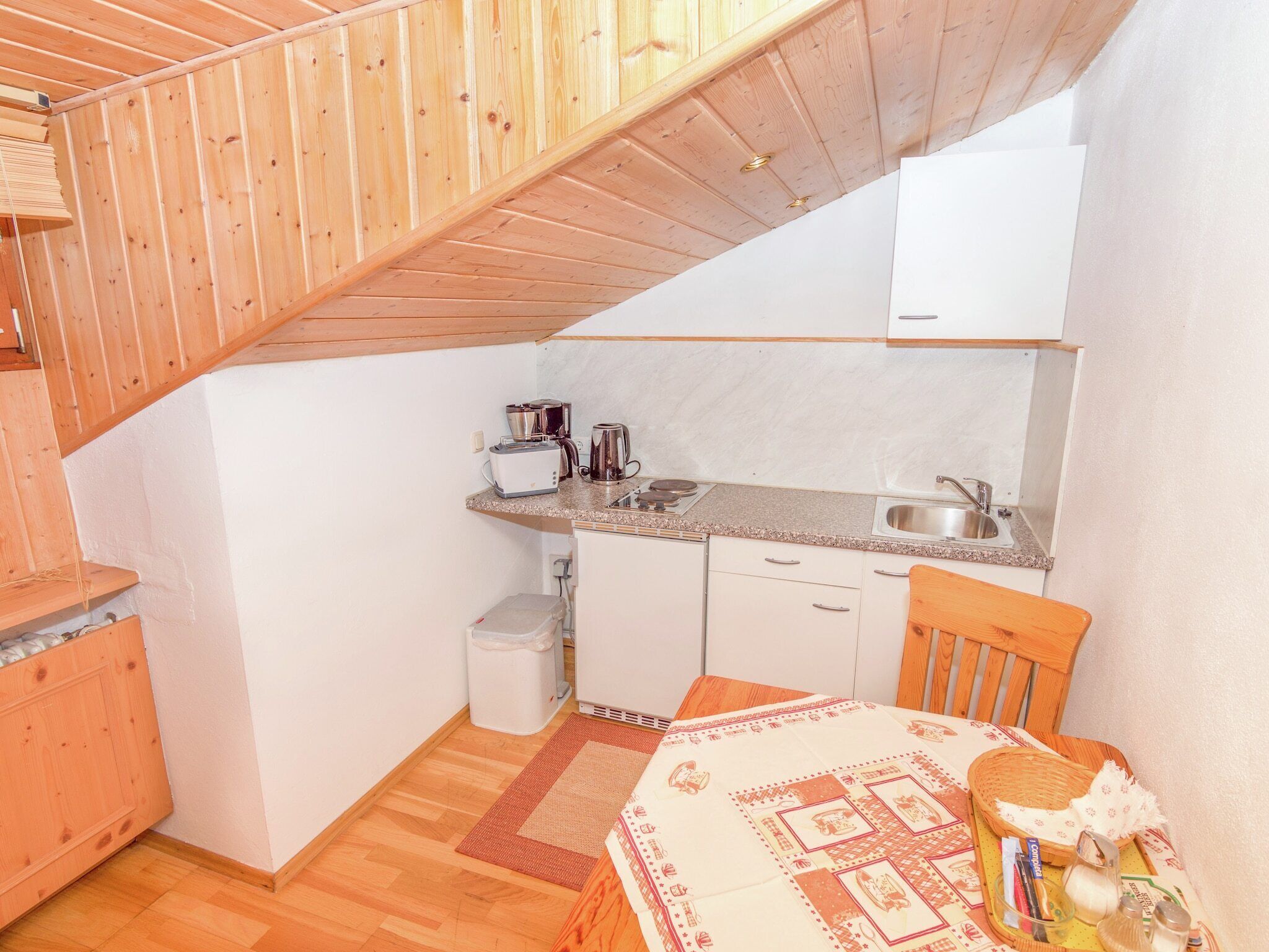A compact kitchen with a wooden ceiling, a sink, a stove, and a small refrigerator.