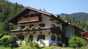 A traditional Alpine-style building with a balcony, surrounded by lush greenery and mountains. - Ferienwohnung in Ruhpolding (Ruhpolding)