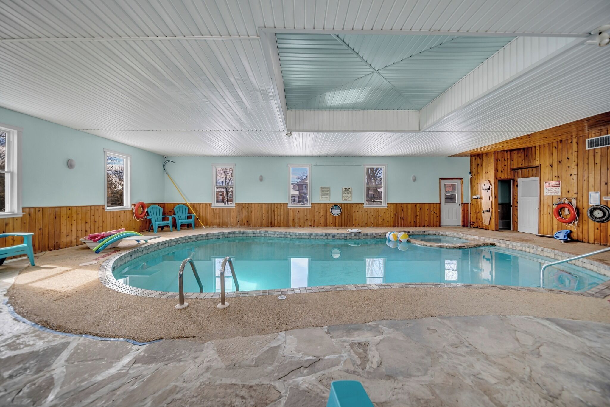 Una piscina interior con revestimiento de madera, suelo de piedra y techo con paneles blancos y azules.