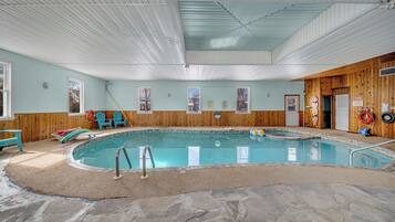 Una piscina interior con revestimiento de madera, suelo de piedra y techo con paneles blancos y azules.