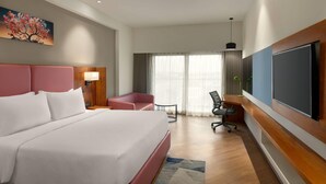 A hotel room with a large bed, a desk, a chair, a TV, and a window with curtains. - Ramada Encore By Wyndham Viramgam (Viramgam)