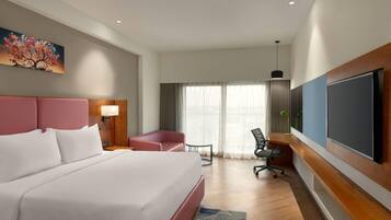 A hotel room with a large bed, a desk, a chair, a TV, and a window with curtains.