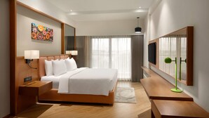 A hotel room with a large bed, a bedside table, a TV, and a window with curtains. - Ramada Encore By Wyndham Viramgam (Viramgam)