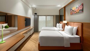 Une chambre d’hôtel avec deux lits, un téléviseur à écran plat, un tableau au mur et une grande fenêtre avec des rideaux.