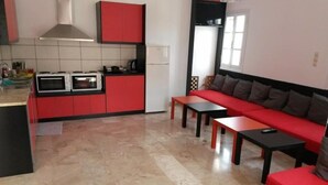 Une cuisine de taille réduite avec des meubles rouges et un plan de travail noir, un canapé rouge agrémenté de coussins et un sol carrelé.