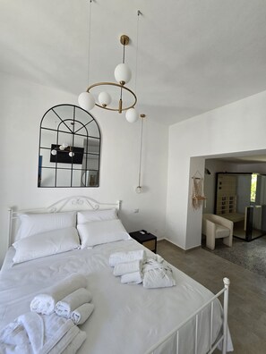 A neatly made bed with white linens and towels, a modern chandelier, a large mirror, and a view into a bathroom with a glass door. - 'ngoppe A Castelluccia (Annunziata)