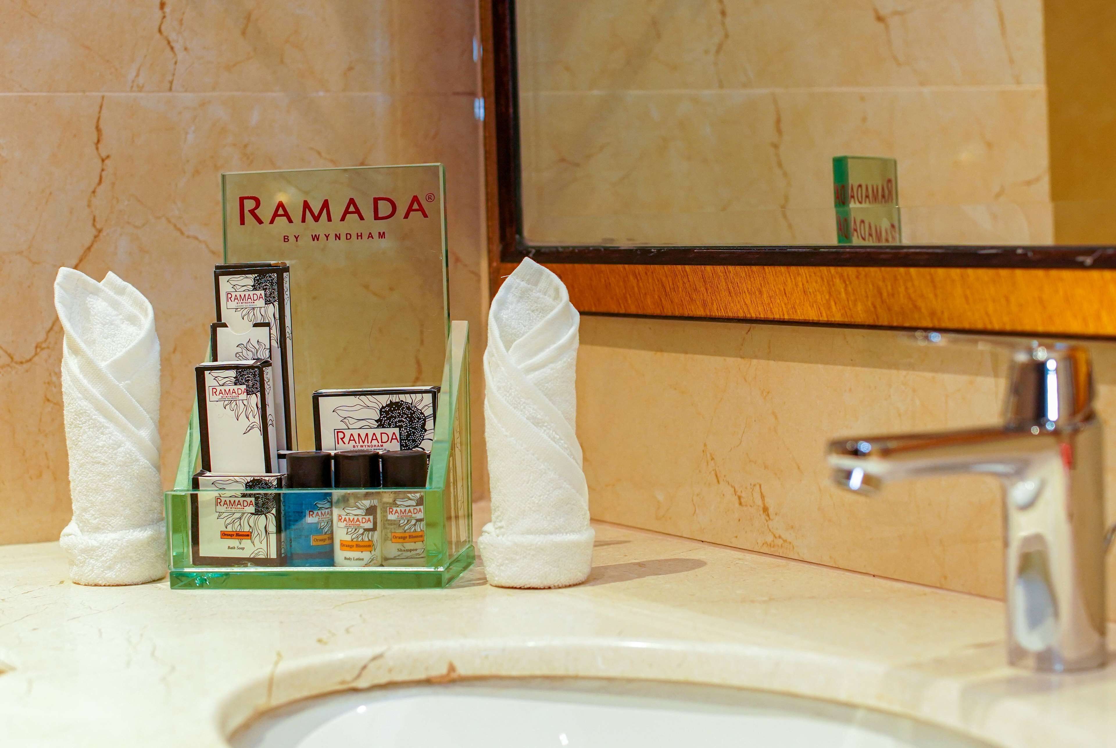 Casa de banho com lavatório de mármore, um frasco de vidro com produtos de higiene pessoal e um espelho a refletir uma garrafa verde.