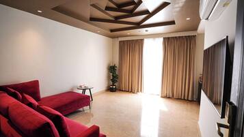 A modern living room with a red sofa, a small table, a potted plant, and a large window with curtains.