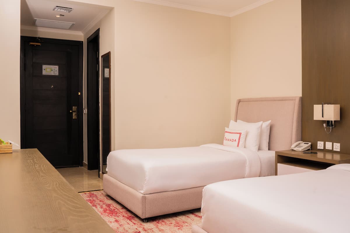 A hotel room with two single beds, a wooden desk, a telephone, and a wall-mounted lamp.